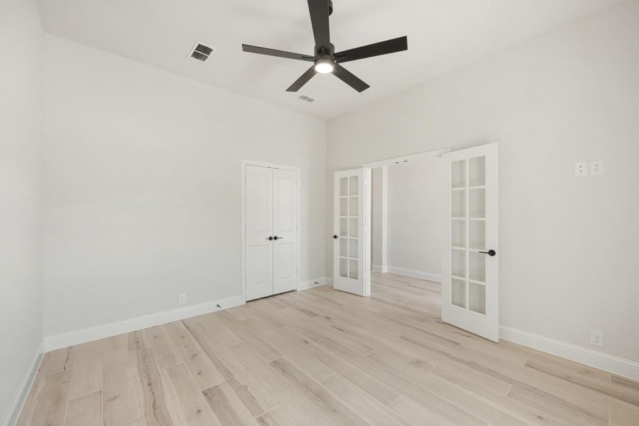 Empty bedroom with light wood floors, black ceiling fan, and white French doors