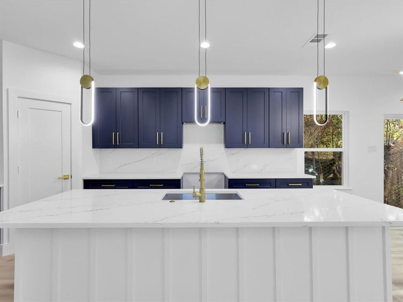 Kitchen featuring blue cabinets, decorative light fixtures, light stone counters, and a kitchen island with sink