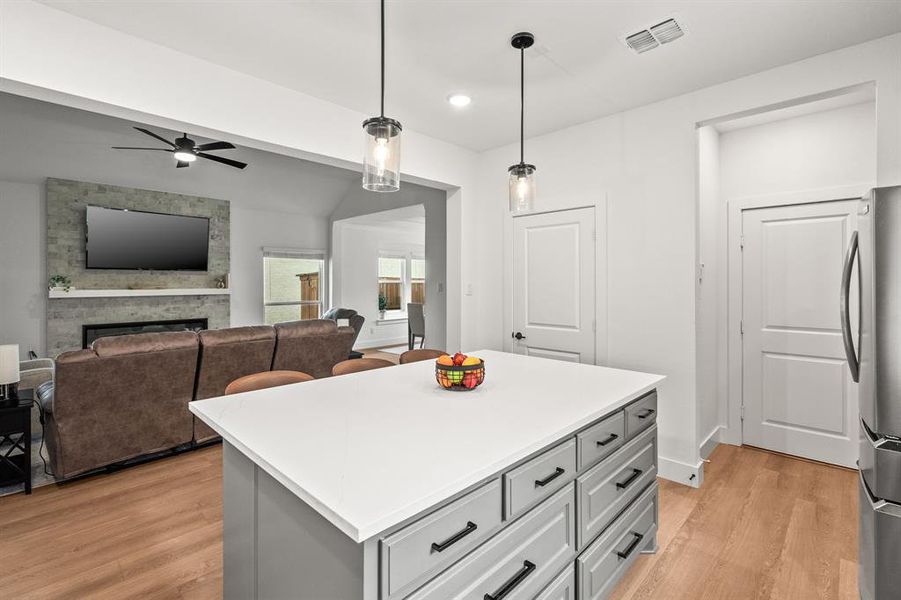 Kitchen with gray cabinets, a stone fireplace, pendant lighting, light wood-type flooring, and a center island Kitchen with gray cabinets, a stone fireplace, pendant lighting, light wood-type flooring, and a center island