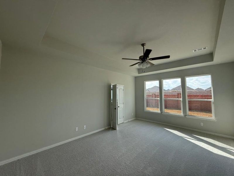 Carpeted empty room with a tray ceiling and a ceiling fan Carpeted empty room with a tray ceiling and a ceiling fan
