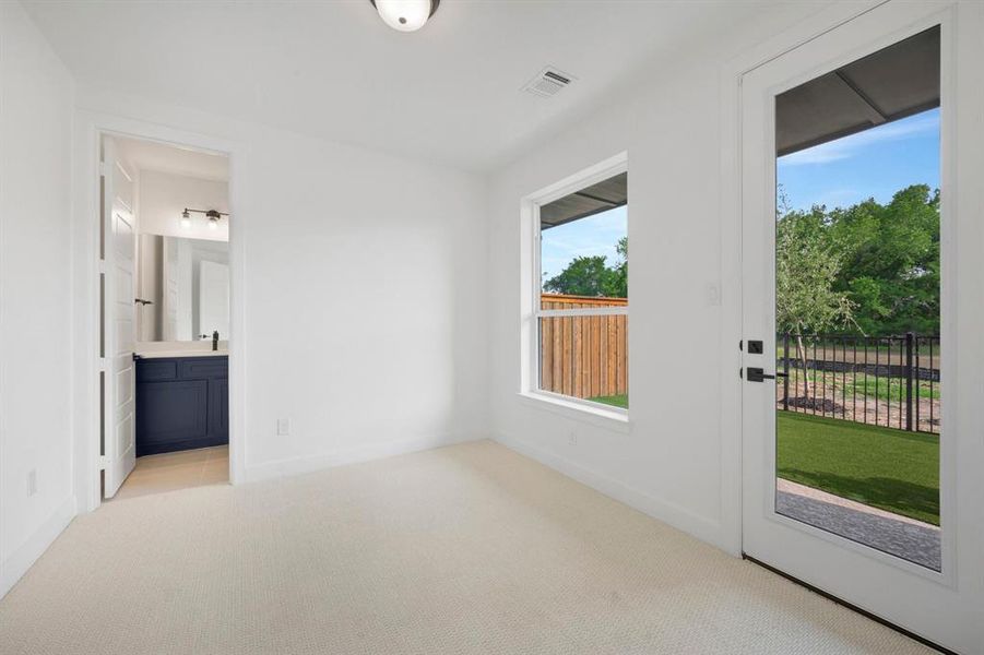 Carpeted room with white walls, featuring a glass-paned door to the exterior and a window with a wooden fence beyond