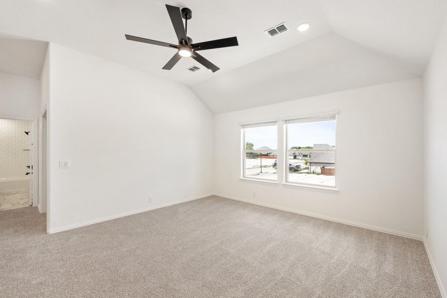 Empty bedroom with vaulted ceiling, ceiling fan, carpet flooring, and ensuite bathroom doorway visible.