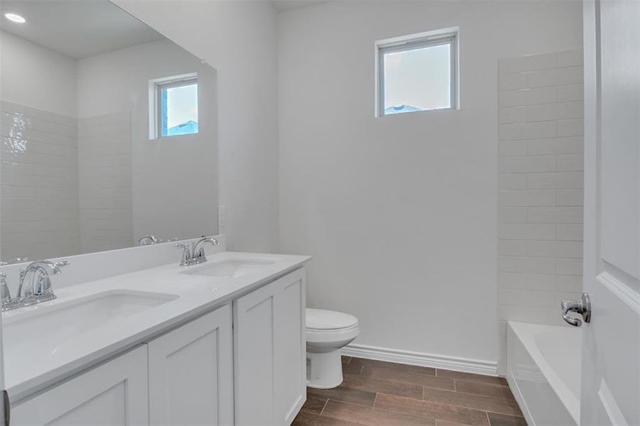 Full bathroom featuring dual vanity, toilet, and bathing tub / shower combination