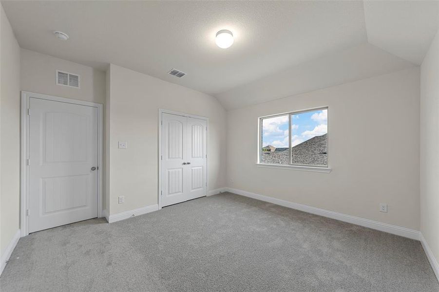 Unfurnished bedroom with light colored carpet, vaulted ceiling, and a closet Unfurnished bedroom with light colored carpet, vaulted ceiling, and a closet