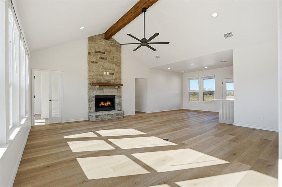 Unfurnished living room featuring a stone fireplace, a ceiling fan, light wood finished floors, high vaulted ceiling, and beam ceiling Unfurnished living room featuring a stone fireplace, a ceiling fan, light wood finished floors, high vaulted ceiling, and beam ceiling