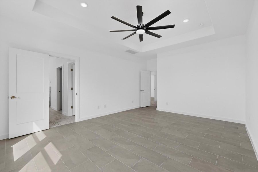 Unfurnished bedroom with ceiling fan, recessed lighting, and a tray ceiling
