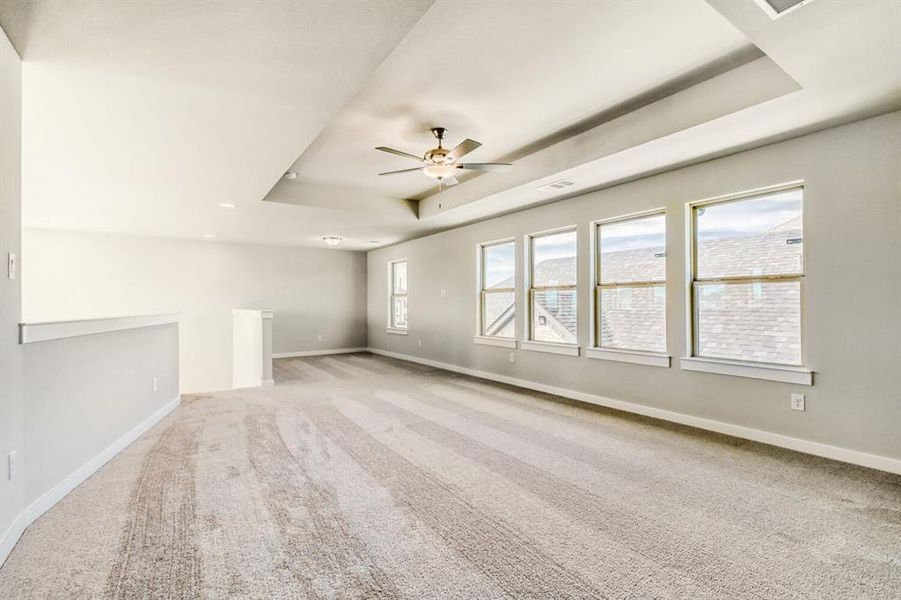Empty room with a tray ceiling, light carpet, and a ceiling fan