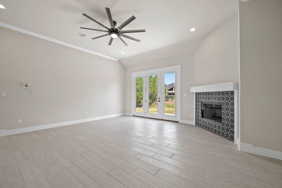 Unfurnished living room with ceiling fan, baseboards, a tile fireplace, french doors, and ornamental molding Unfurnished living room with ceiling fan, baseboards, a tile fireplace, french doors, and ornamental molding