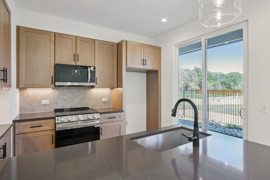 Kitchen with stainless steel appliances, dark stone counters, decorative backsplash, recessed lighting, and decorative light fixtures