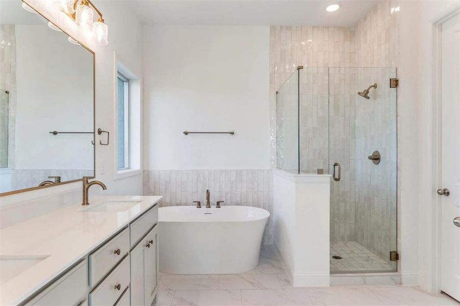 Bathroom with a freestanding bath, a stall shower, double vanity, a wainscoted wall, and light marble finish floors