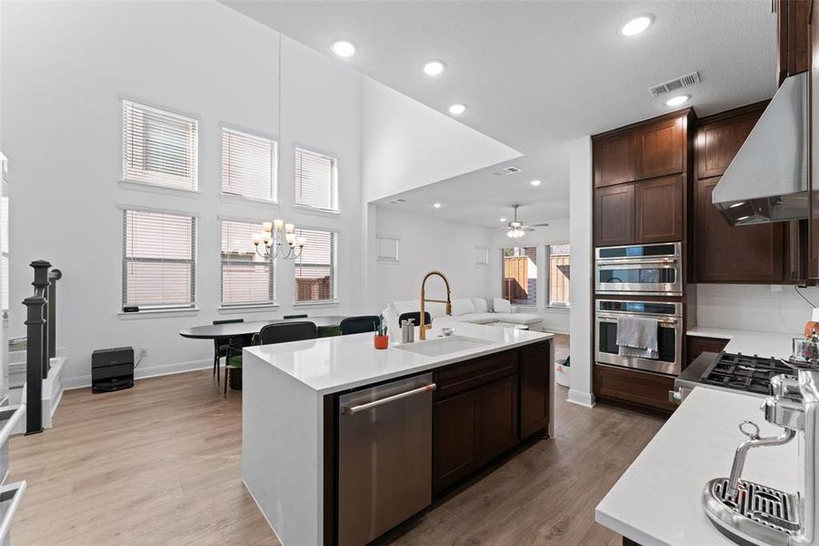 Kitchen with dark brown cabinetry, light stone countertops, open floor plan, appliances with stainless steel finishes, and recessed lighting Kitchen with dark brown cabinetry, light stone countertops, open floor plan, appliances with stainless steel finishes, and recessed lighting