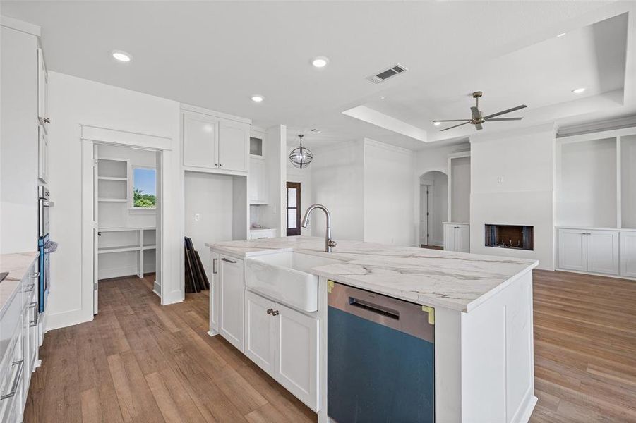 Open-concept kitchen and living area featuring a large center island with a farmhouse sink, stainless steel dishwasher, and stone-finish countertop