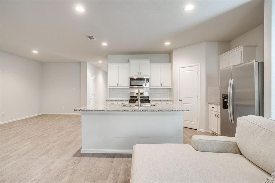 Kitchen featuring stainless steel appliances, tasteful backsplash, white cabinets, light stone counters, and recessed lighting
