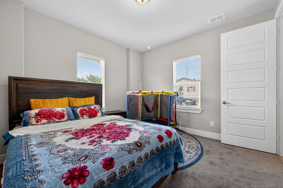 This room features carpeted flooring, a dark wood headboard, and two windows providing natural light