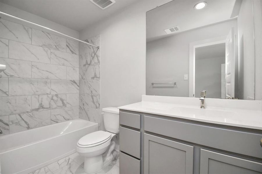 Experience sophistication in the secondary bathroom, where tile flooring complements a bath/shower combo with tile surround. Light wood cabinets enhance the space, while a distinctive barrel ceiling adds a touch of architectural elegance. Complete with a beautiful light countertop, this bathroom Sample photo of completed home with similar floor plan. As-built interior colors and selections may vary.