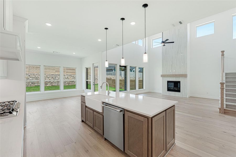 Open-concept kitchen with large island, farmhouse sink, pendant lights, and fireplace in adjoining living area with high ceilings.