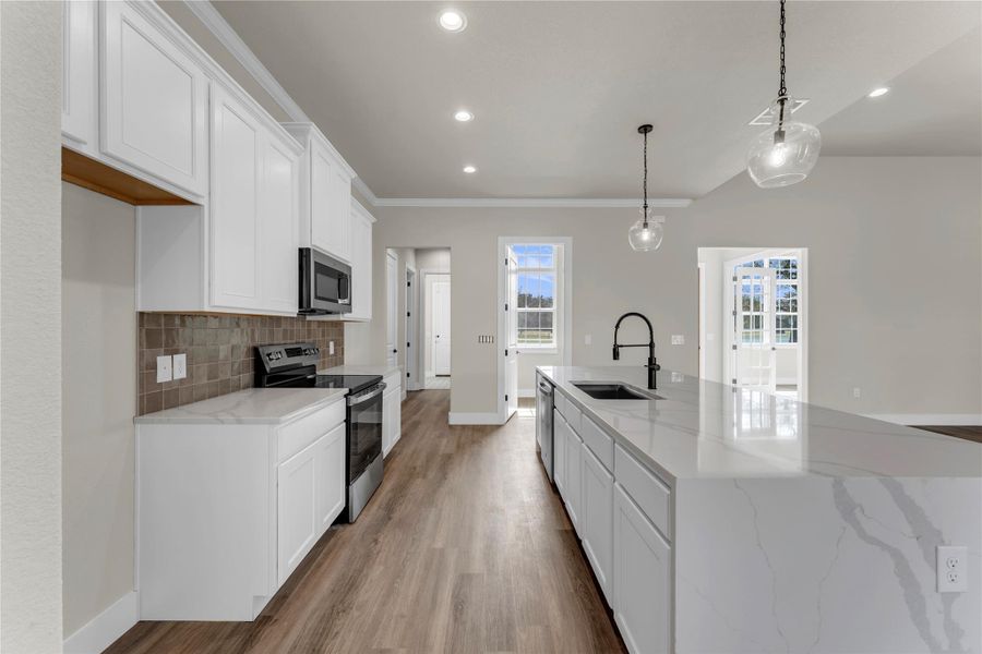 Kitchen featuring white cabinetry, stainless steel appliances, light stone countertops, tasteful backsplash, and a center island with sink