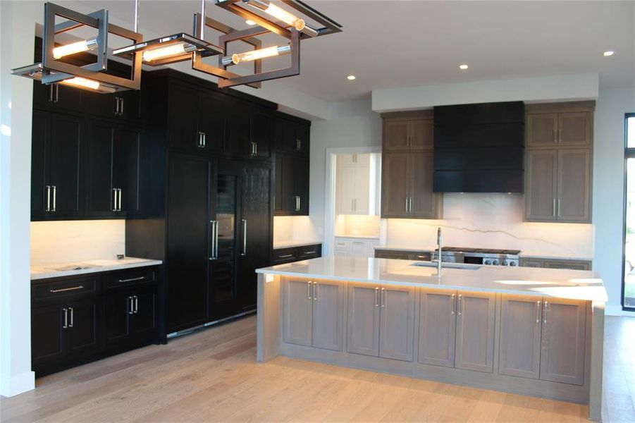 Kitchen with premium range hood, a kitchen island with sink, sink, and light hardwood / wood-style floors