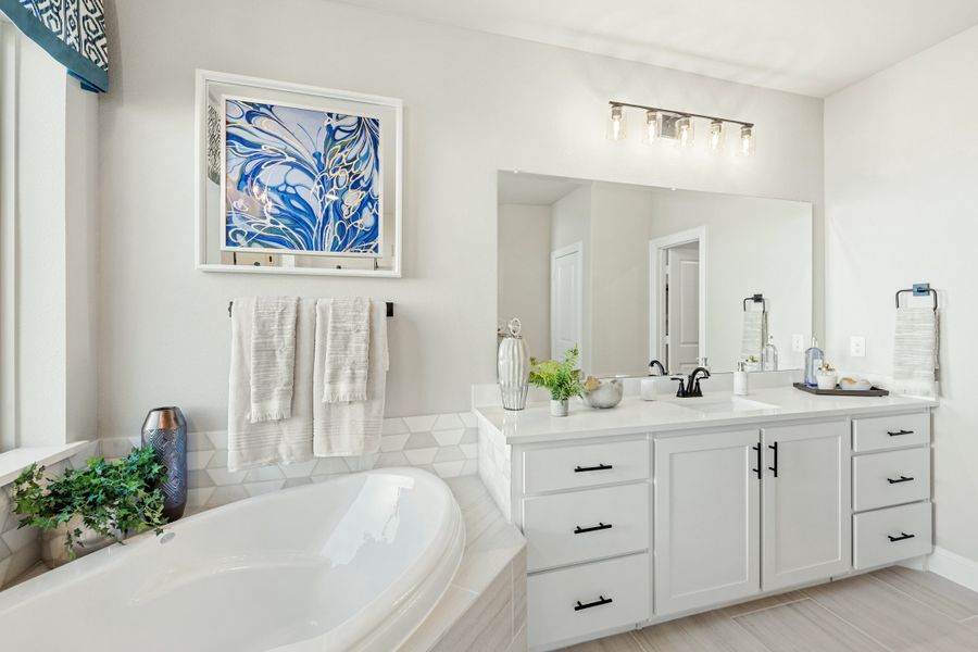 Master bathroom with soaking tub, white double vanity, large mirror, and modern light fixture above sink. Master bathroom with soaking tub, white double vanity, large mirror, and modern light fixture above sink.