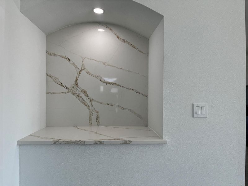 This photo showcases a stylish recessed quartz niche with elegant veining, illuminated by a built-in spotlight, and adjacent to a modern light switch. Perfect for displaying decorative items or art.