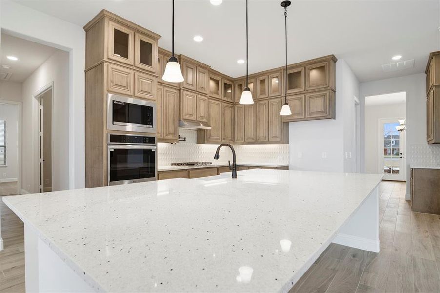 Kitchen featuring decorative backsplash, appliances with stainless steel finishes, under cabinet range hood, a sink, and light wood-type flooring