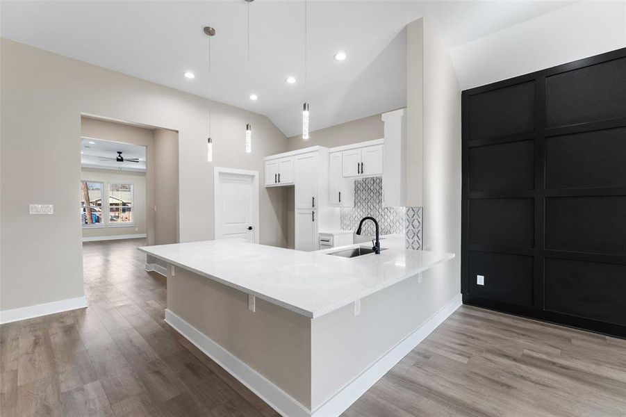 Kitchen with sink, light hardwood / wood-style flooring, white cabinetry, hanging light fixtures, and tasteful backsplash