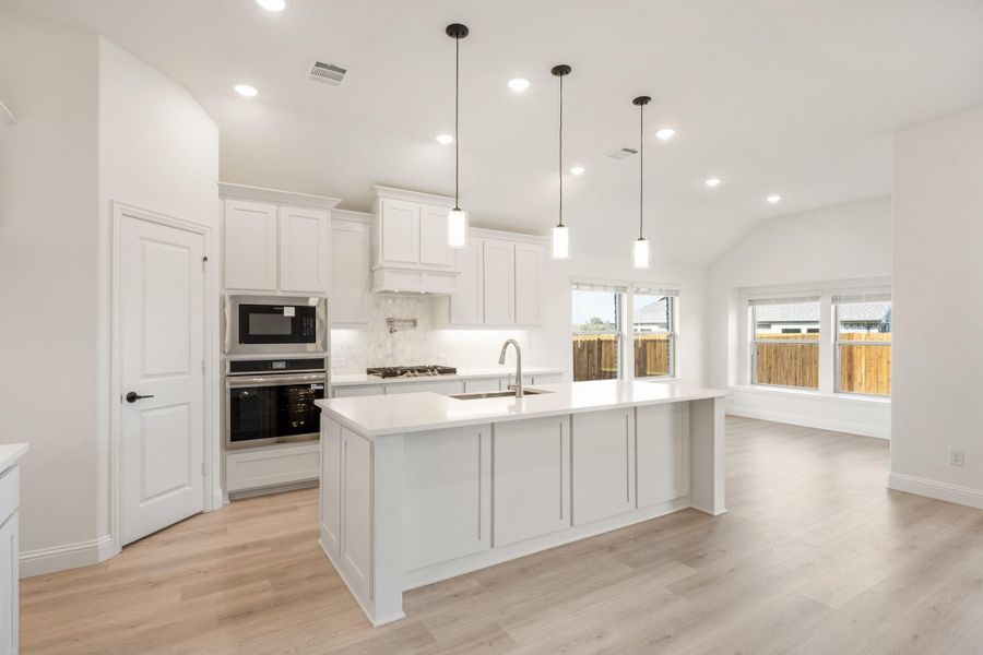 Open kitchen with white cabinets, large island, pendant lights, and stainless steel appliances on light hardwood floors Open kitchen with white cabinets, large island, pendant lights, and stainless steel appliances on light hardwood floors