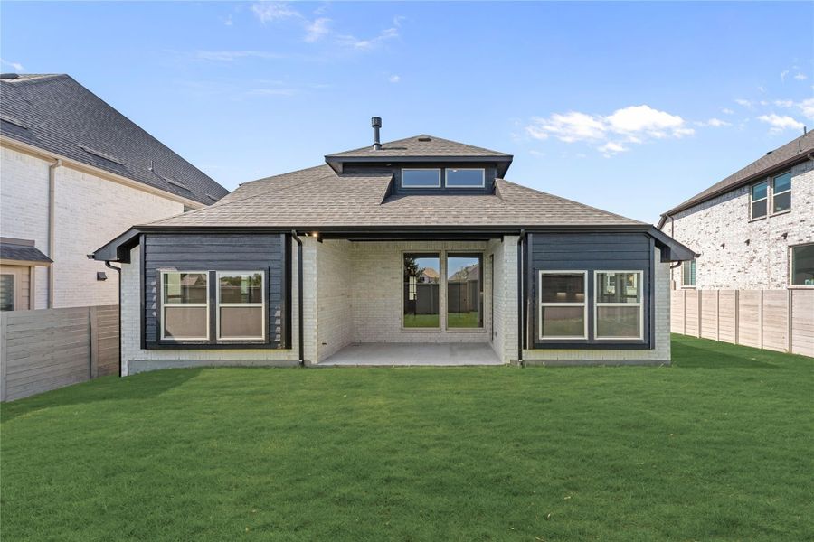 Rear exterior of single-story home with dark siding, brick accents, covered patio, and green backyard lawn.