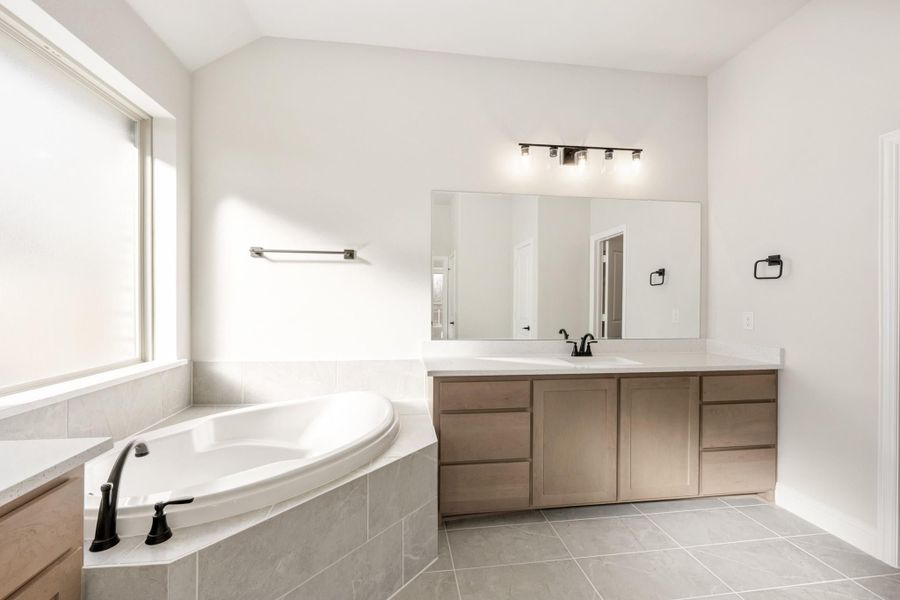 Master bathroom with corner soaking tub, single-sink vanity, and large mirror with light bar above