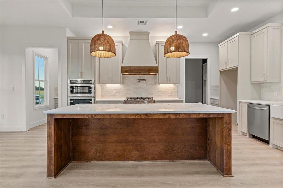 Kitchen featuring a kitchen island, tasteful backsplash, light stone counters, hanging light fixtures, and stainless steel appliances Kitchen featuring a kitchen island, tasteful backsplash, light stone counters, hanging light fixtures, and stainless steel appliances