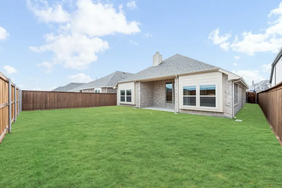 Backyard of brick home with large green lawn, wood privacy fence, and small covered patio Backyard of brick home with large green lawn, wood privacy fence, and small covered patio