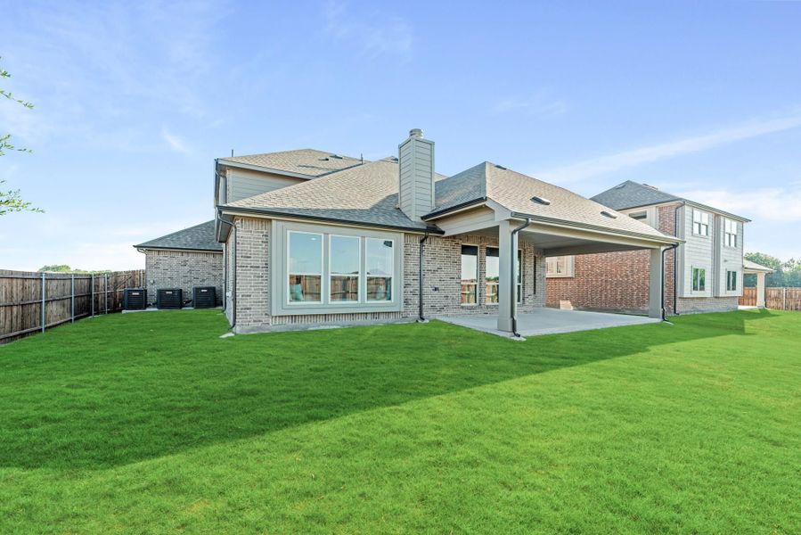 Rear exterior of brick home with covered patio, large backyard, and wood privacy fence