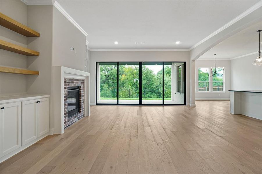 Unfurnished living room with light hardwood / wood-style floors, a notable chandelier, and ornamental molding