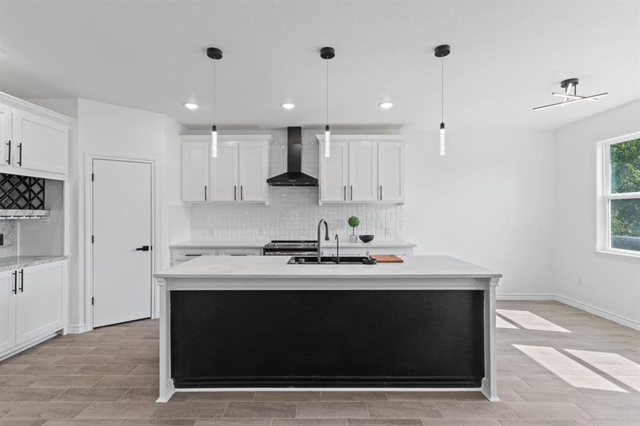 Kitchen featuring white cabinets, a center island with sink, and backsplash