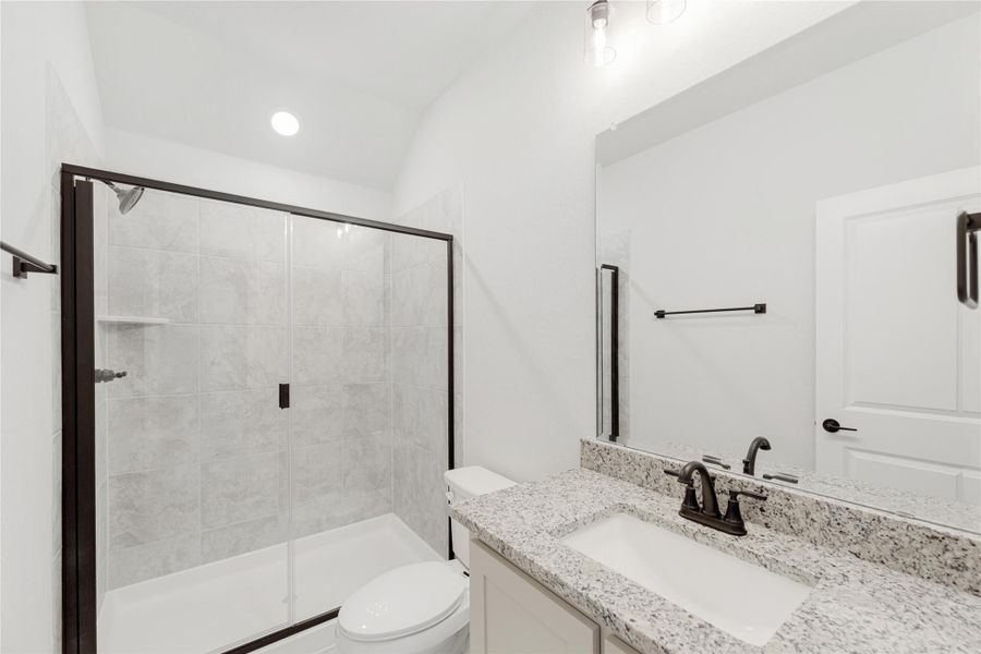 Bathroom with granite vanity, glass-enclosed tile shower, and white toilet with dark bronze fixtures Bathroom with granite vanity, glass-enclosed tile shower, and white toilet with dark bronze fixtures