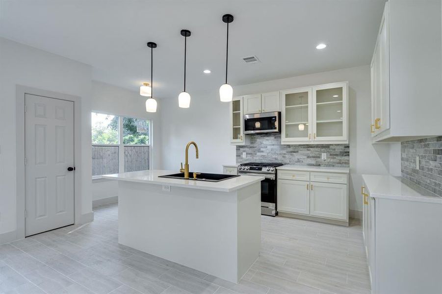 Kitchen with white cabinetry, appliances with stainless steel finishes, sink, and an island with sink