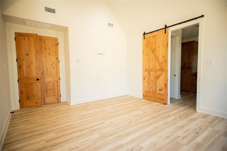Unfurnished room with a barn door, visible vents, and light wood-style floors Unfurnished room with a barn door, visible vents, and light wood-style floors
