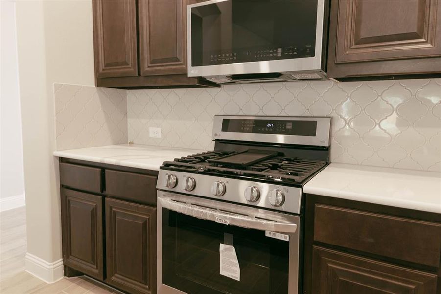 Kitchen with tasteful backsplash, light hardwood / wood-tile style flooring for that active family, stainless steel appliances, and dark brown cabinetry