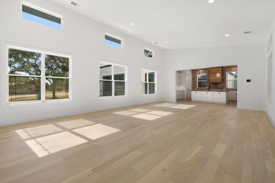 Unfurnished living room with a high ceiling, healthy amount of natural light, light wood finished floors, and recessed lighting