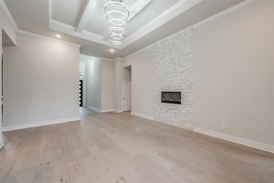 Unfurnished living room featuring recessed lighting, light wood-type flooring, ornamental molding, a fireplace, and a chandelier