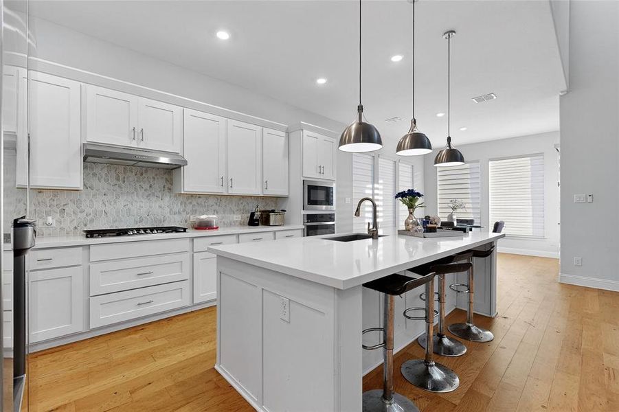 Kitchen featuring backsplash, light wood-style floors, a breakfast bar, white cabinetry, and an island with sink