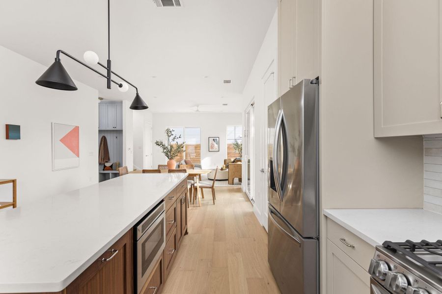 Kitchen featuring light wood-style flooring, stainless steel appliances, decorative light fixtures, a kitchen island, and light stone countertops Kitchen featuring light wood-style flooring, stainless steel appliances, decorative light fixtures, a kitchen island, and light stone countertops