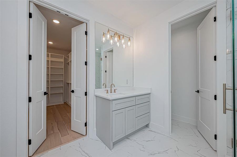 Features a sleek vanity with a large mirror and stylish lighting. There's access to a spacious walk-in closet with ample shelving through double doors.