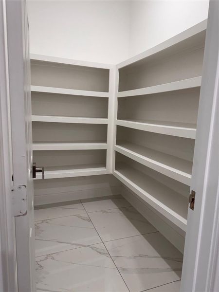 Spacious walk-in pantry featuring elegant tile flooring and ample shelving for organized storage. Spacious walk-in pantry featuring elegant tile flooring and ample shelving for organized storage.