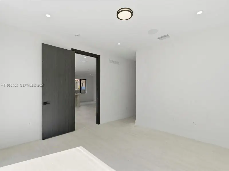 Interior space featuring light wood-finish flooring, charcoal-toned door with matte black hardware, recessed ceiling lighting, and a circular flush-mount fixture Interior space featuring light wood-finish flooring, charcoal-toned door with matte black hardware, recessed ceiling lighting, and a circular flush-mount fixture