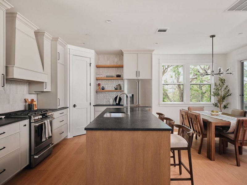 Kitchen featuring an island with sink, stainless steel appliances, light wood-style floors, open shelves, and decorative backsplash