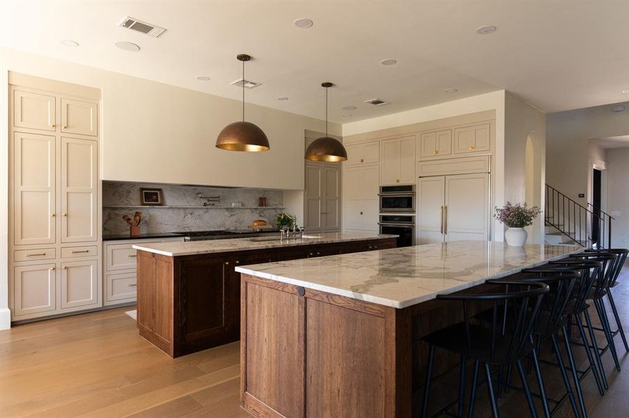 Two tone kitchen with light stone counters, light wood-type flooring, a breakfast bar, backsplash, and two tone color scheme