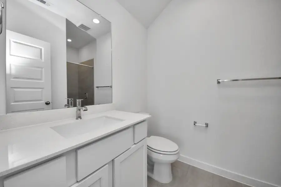 Secondary bath features tile flooring, walk-in shower with tile surround, light stained wood cabinets, beautiful light countertop. Sample photo of completed home with similar floor plan. Actual colors and selections may vary.