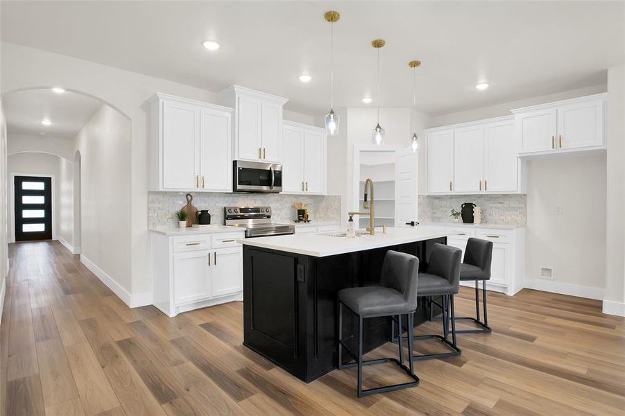 Kitchen featuring white cabinets, light hardwood / wood-style floors, stainless steel appliances, and an island with sink