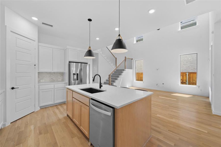 Open-concept living space featuring a central kitchen island with a black sink and faucet, integrated dishwasher, and pendant lighting